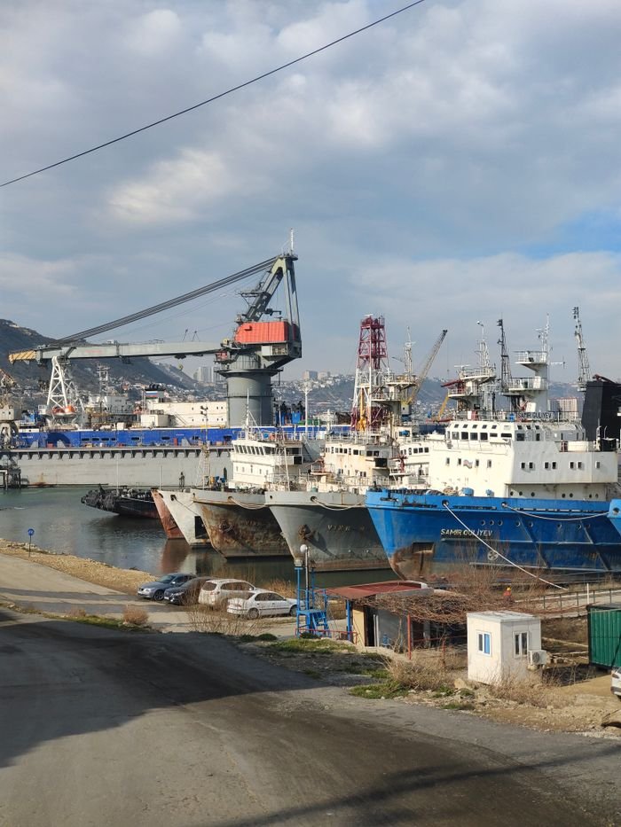A busy industrial harbor with docked cargo ships and towering cranes under a partly cloudy sky.
