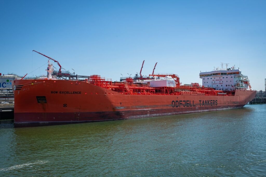 A large red oil tanker named Bow Excellence docked at a harbor under clear blue skies.