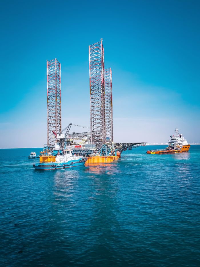 Offshore oil rig and support vessels in Ras Laffan, Qatar under clear blue sky.